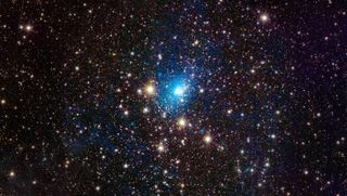 Coulntless stars and points of light in black space. In the center, a bright blue light shiens, radiating outward a faint blue hue.